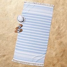 a blue and white beach towel, hat, flip flops on the sand