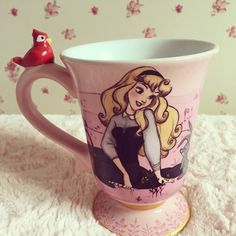 a pink coffee cup with a drawing of a girl on the side and a red bird perched on top