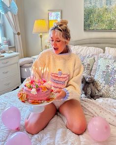 a woman sitting on her bed holding a birthday cake with lit candles and pink balloons