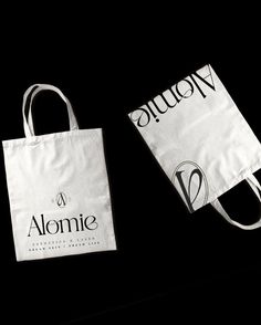 two white shopping bags sitting next to each other on top of a black surface with the word alquon printed on it