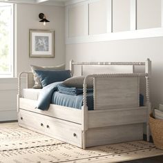 a white bed with blue pillows on top of it in a room next to a window