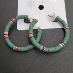 two green and gold hoop earrings sitting on top of a white plastic card with a black background