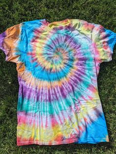 a tie - dyed t - shirt laying on the grass with it's back to the camera