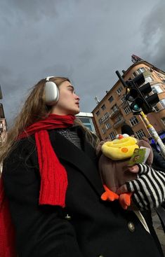 a woman wearing headphones and holding a stuffed duck in her hand while standing on the street