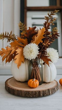 some white pumpkins and flowers in a glass jar on a wood slice with leaves