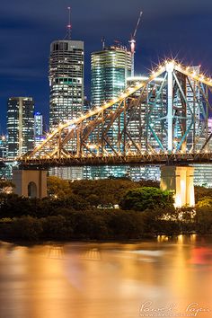 the city skyline is lit up at night as seen from across the water with a bridge in the foreground