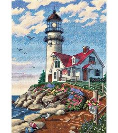 someone holding up a cross - stitch picture of a lighthouse on the coast with flowers