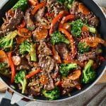 a skillet filled with beef and broccoli on top of a wooden table