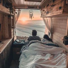 a person laying in bed looking out at the ocean from inside a truck with its door open