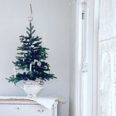 a small christmas tree sitting on top of a white table next to a window in a room