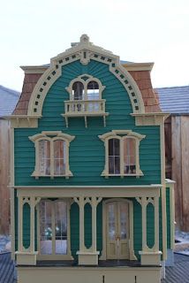 a doll house is shown in front of a wooden fence and building with two windows