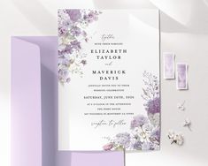 the wedding stationery is laid out on top of purple and white paper with flowers