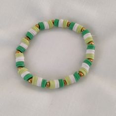 a green and white beaded bracelet on a white cloth covered table with a gold - plated clasp