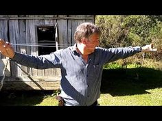 an older man is holding his arms out in front of a wooden building with barbed wire on it