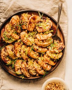 a pan filled with chicken and vegetables next to a bowl of nuts on a table