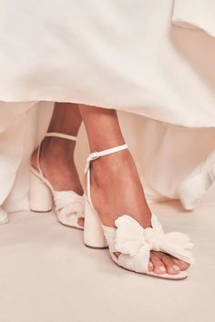 a bride's feet in white shoes with a bow on the side and her wedding dress