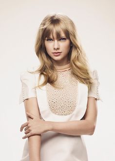 a woman with blonde hair wearing a white dress and holding her arms crossed in front of her chest