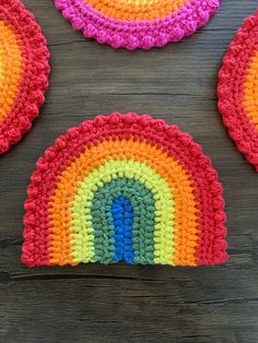 three crocheted rainbow coasters sitting on top of a wooden table