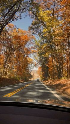 a car driving down a road surrounded by trees in the fall time with leaves on the ground