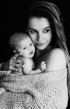 a woman is holding a baby wrapped in a blanket and posing for a black and white photo