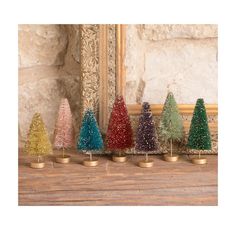 small christmas trees lined up in front of a gold framed mirror on a wooden table