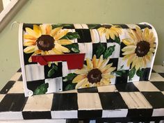 a painted mailbox sitting on top of a checkered table with sunflowers