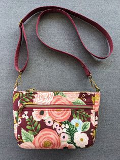 a floral purse on a gray surface with a red strap and two small flowers in the middle