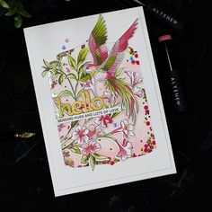 a card with an image of a bird and flowers on it, next to a pen