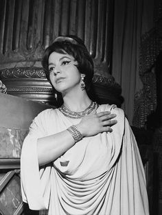 black and white photograph of woman in dress with bracelets on her neck, standing next to column