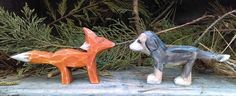 two small ceramic foxes sitting on top of a stone slab next to pine needles and branches