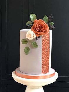 a white and gold wedding cake with flowers on the top is sitting on a pedestal