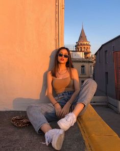 a woman sitting on the ground with her legs crossed, wearing sunglasses and a tank top