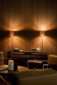 a dimly lit room with two lamps on the wall and leather chairs in the foreground