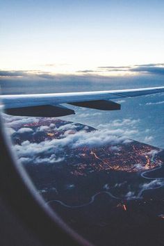 the wing of an airplane as seen from above in flight over clouds and land at night