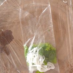 a plastic bag filled with lettuce on top of a wooden table