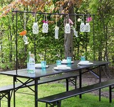 a picnic table set up outside with flowers hanging from the branches and plates on it