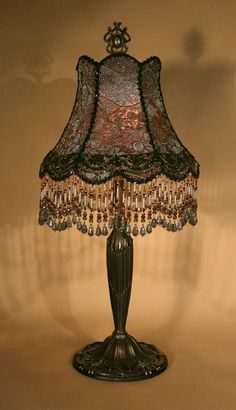 a lamp that is on a table with a brown shade over the base and beaded lampshade