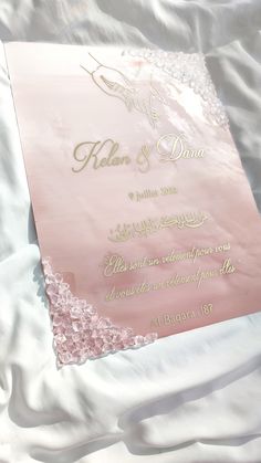 the wedding card is laying on top of the white sheet with pink and gold lettering