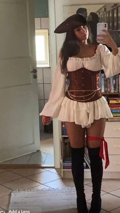 a woman in a pirate costume taking a selfie with her cell phone while standing next to a bookshelf