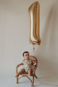 a baby sitting in a chair next to a balloon