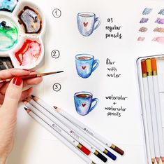 a woman's hand holding a paintbrush next to some watercolor pencils