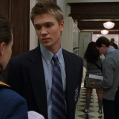 a young man in a suit and tie standing next to another person wearing a blue shirt and black blazer