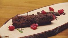 a piece of chocolate cake with raspberries on it sitting on a wooden cutting board