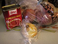 some food is sitting on the table next to a can of corned beef and hot dog buns