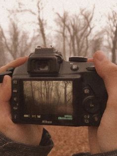 a person holding up a camera to take a photo in front of some trees with no leaves