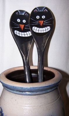 two wooden spoons with faces painted on them sitting in a ceramic pot filled with water