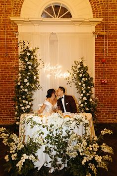 a bride and groom kissing in front of a table with flowers on it at their wedding reception