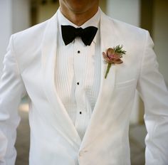 a man wearing a white suit with a black bow tie and flower in his lapel