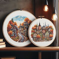 two cross - stitch pictures on a shelf with some books and lightbulbs