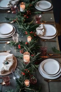 the table is set for christmas dinner with candles and greenery on it's side